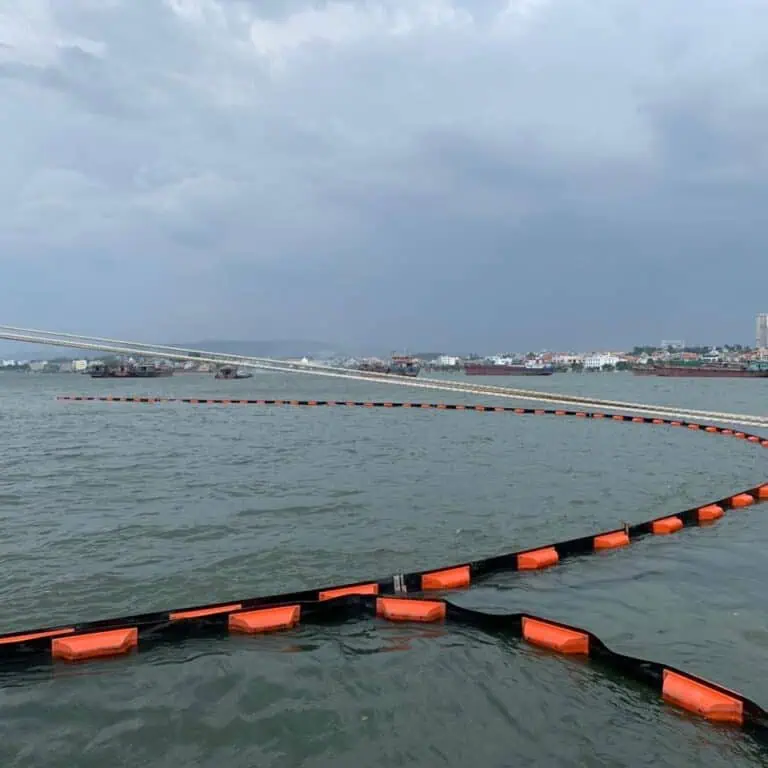 Floating barrier in water with city in background.