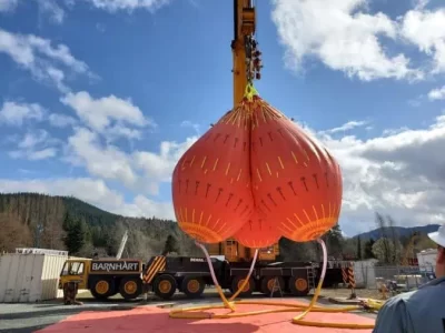 Large orange tensile structure being lifted by crane.