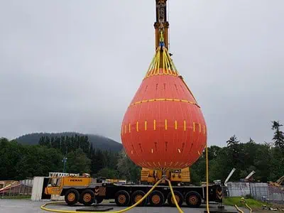 Large orange water balloon hanging from crane.