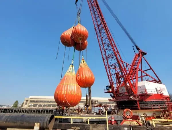 Crane lifting large orange crane test water bags at a construction site.