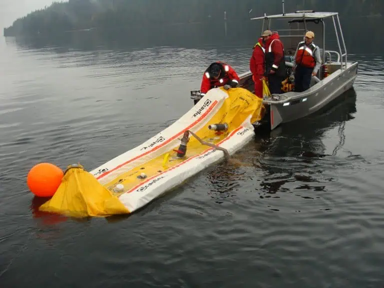 Workers deploy oil spill containment boom from boat.