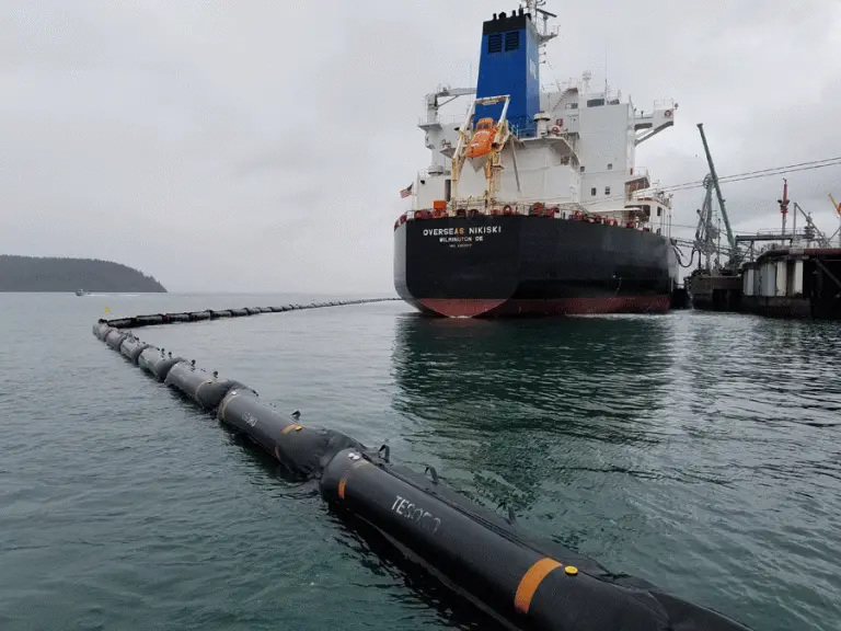 Large cargo ship docked at pier with barrier.