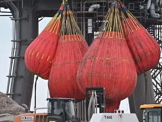 Large red industrial lifting crane test water bags suspended on crane.