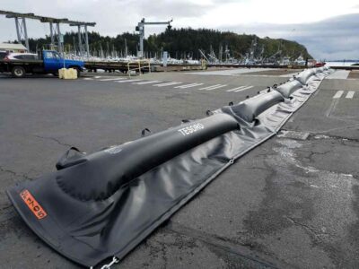 Inflatable barrier on harbor dock with boats.