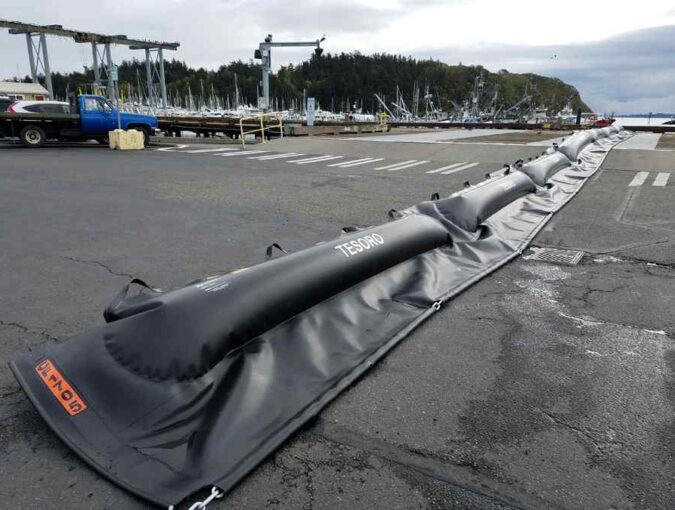 Inflatable barrier on harbor dock with boats.