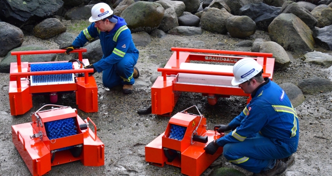 Workers operating orange beach cleaning machines