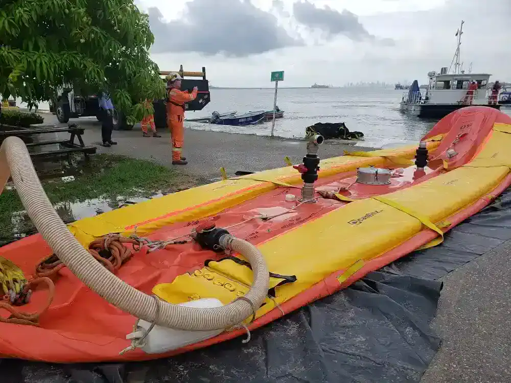 Workers preparing oil spill containment boom near shore