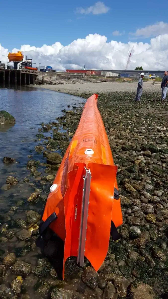 Orange flood barrier deployed on rocky shoreline