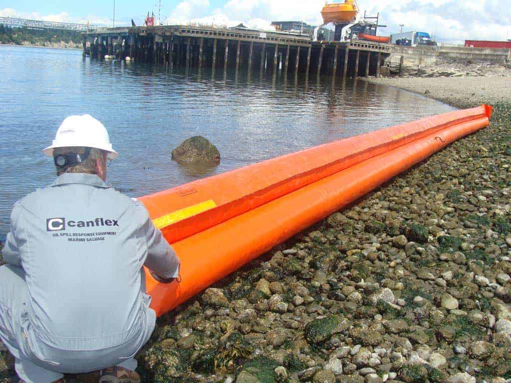 Worker installing orange oil spill containment boom