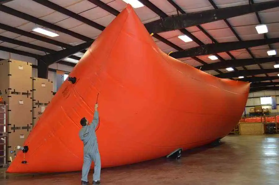 Worker inspecting large orange inflatable tank indoors