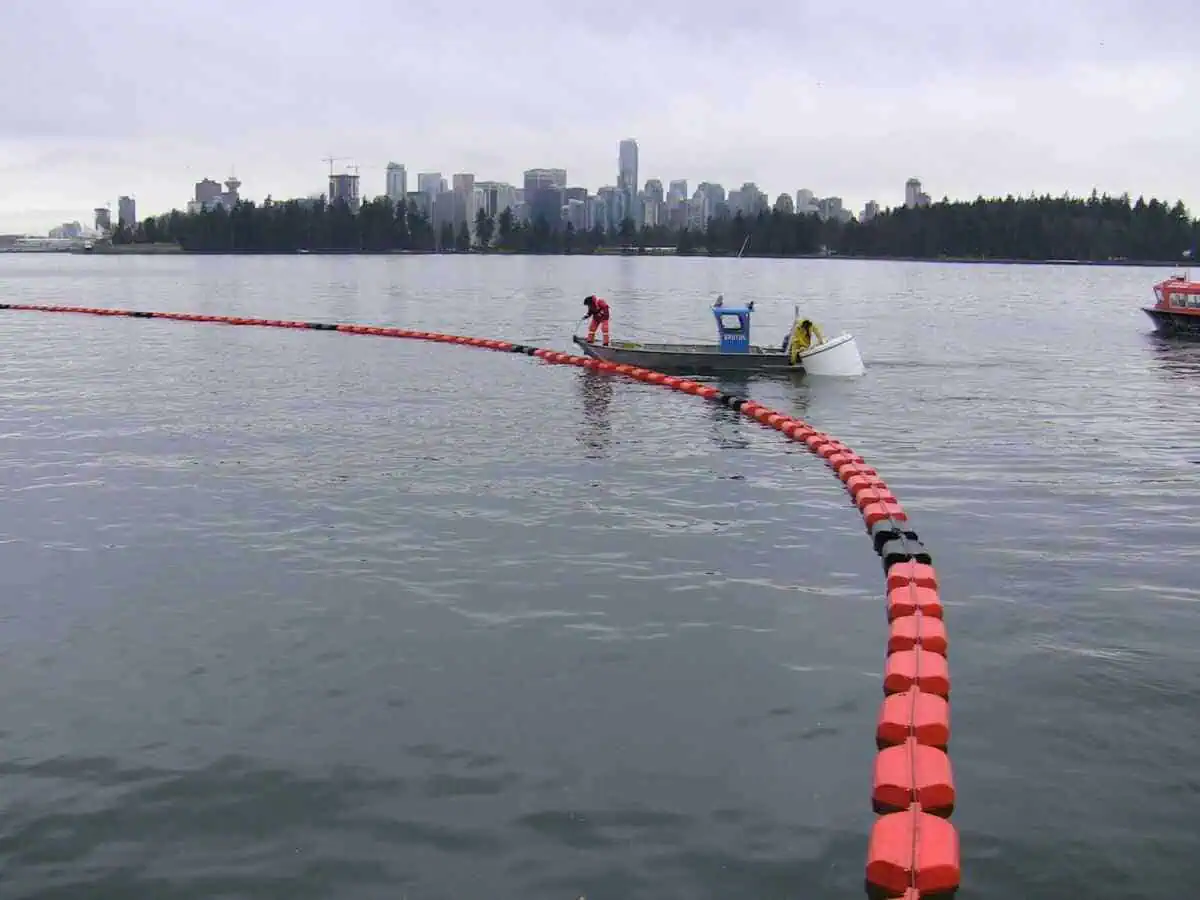 Boat deploying floating barrier near city shoreline