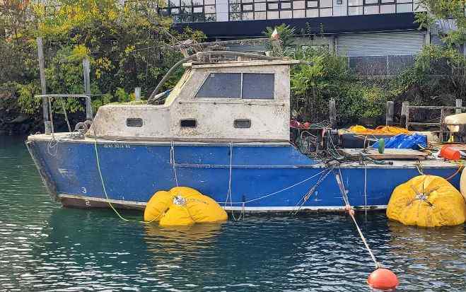 Old blue boat floating with yellow buoys
