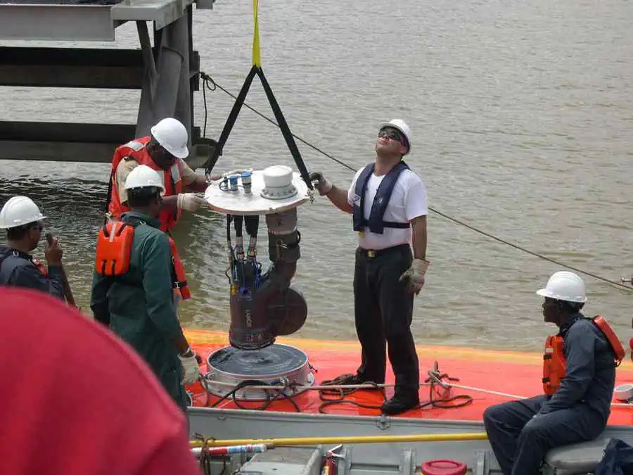 Workers install equipment on floating platform near water.
