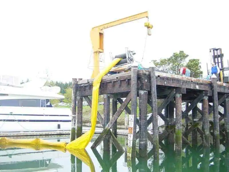 Workers deploying yellow boom from dock crane