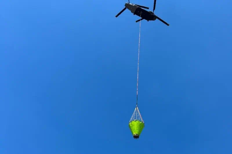 Helicopter carrying green water bucket in sky