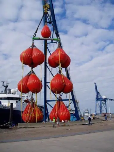 Crane lifting large red water bags at dockyard