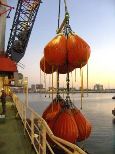 Crane lifting large orange water bags over ship deck