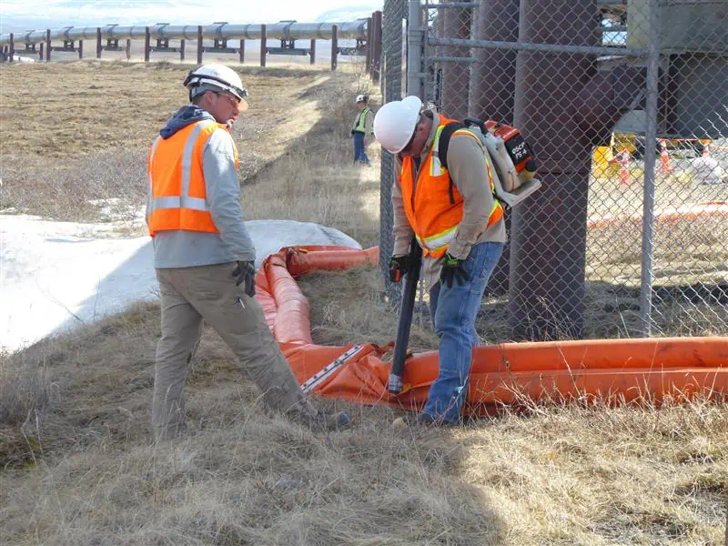 Workers installing orange pipeline barrier outdoors